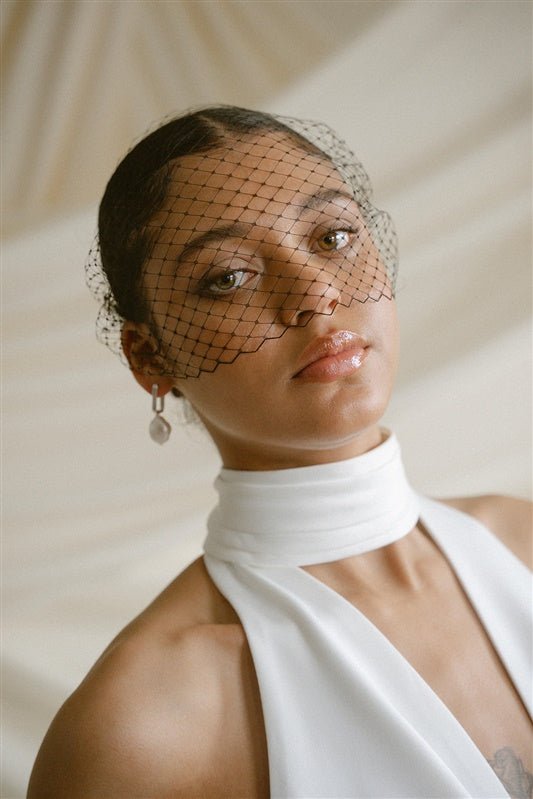 Black bride wears a black Birdcage Veil with statement pearl earrings and a halterneck wedding dress.