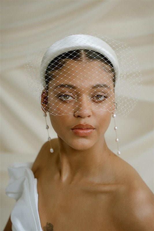 A black bride wears a full gathered birdcage veil with an ivory satin padded headband and statement long drop baroque pearl earrings