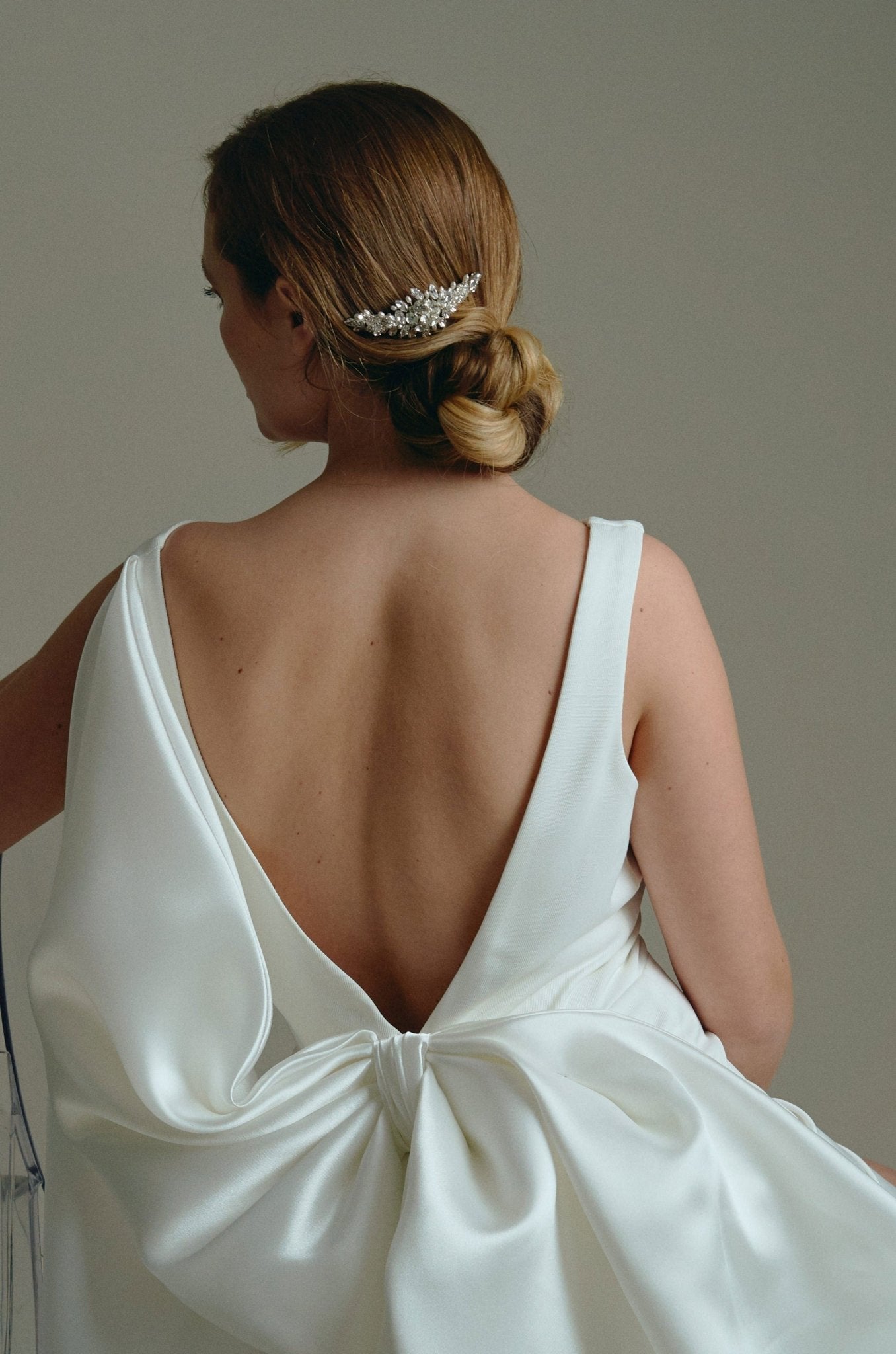 Bridal hair comb with silver crystals and freshwater pearls worn by a bride with a low bun updo and wearing a statement bow bridal gown