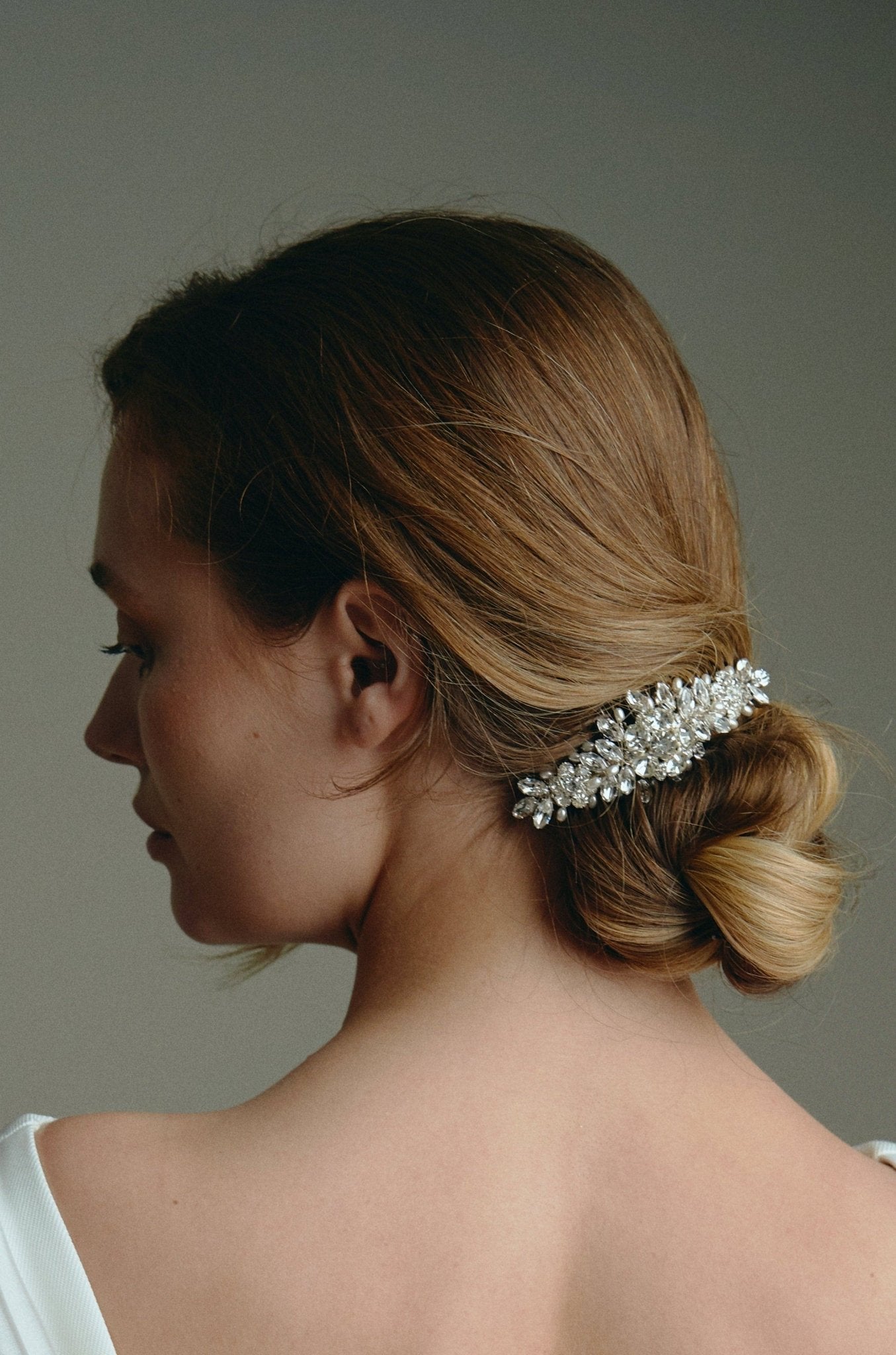 Bridal hair comb with silver crystals and freshwater pearls worn by a bride with a low bun updo and wearing a statement bow bridal gown
