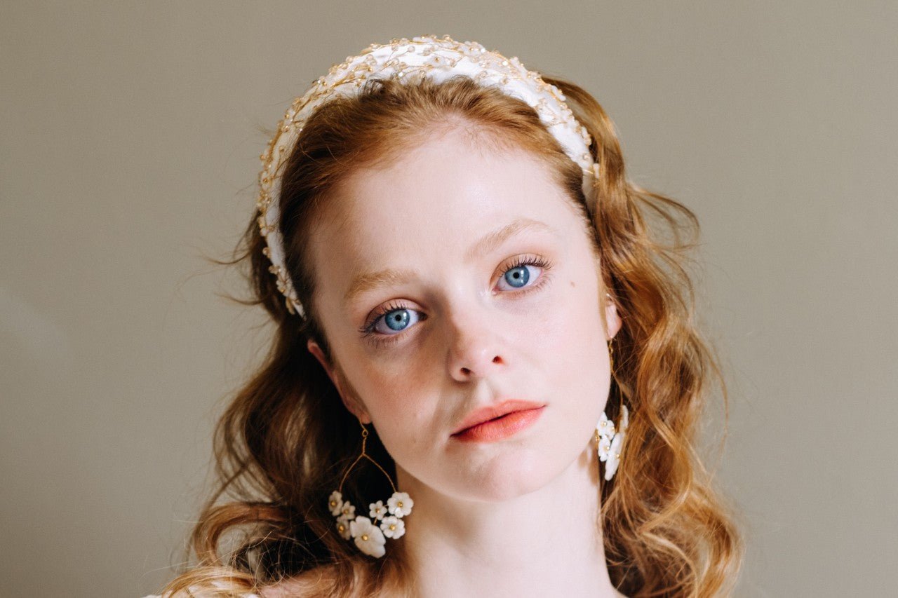 redheaded model wears ivory padded headband with gold floral embellishment and matching floral hoop earrings