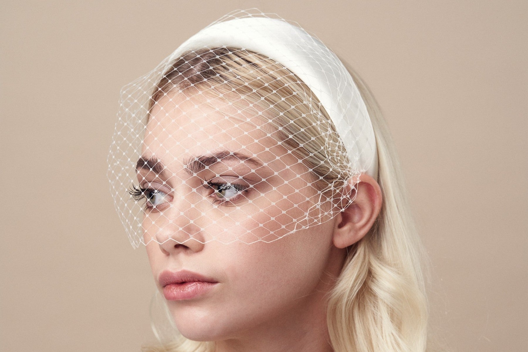 Blonde model wears ivory padded headband with adjustable birdcage veil attached