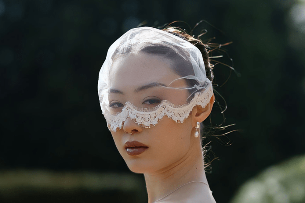 Bride wears a micro veil made of tulle covering half the face with a lace edge finish