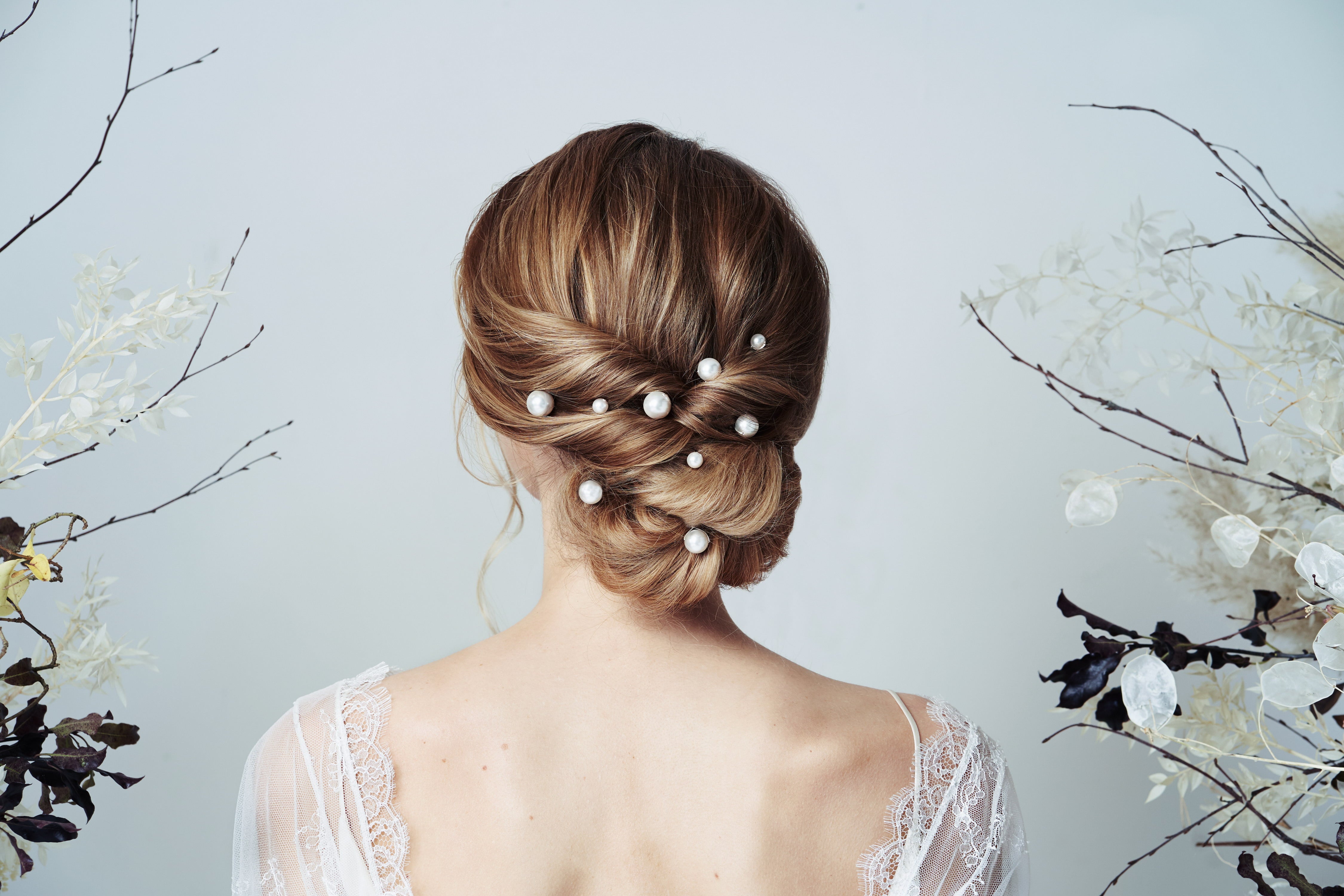 Bride wears single pearl hairpins in mixed sizes scattered through a twisted low bun updo