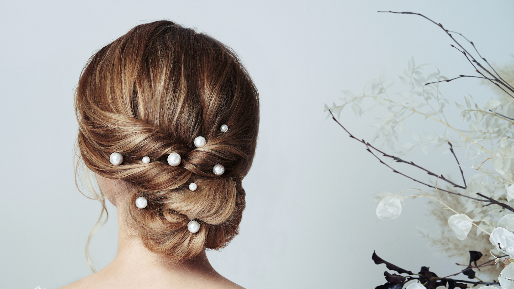 Model with twisted low bun wears a set of nine scattered pearl hairpins in three sizes, small, medium and large