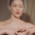 bride wears a sheer tulle birdcage style veil with long drop pearl earrings and a baroque coin pearl necklace
