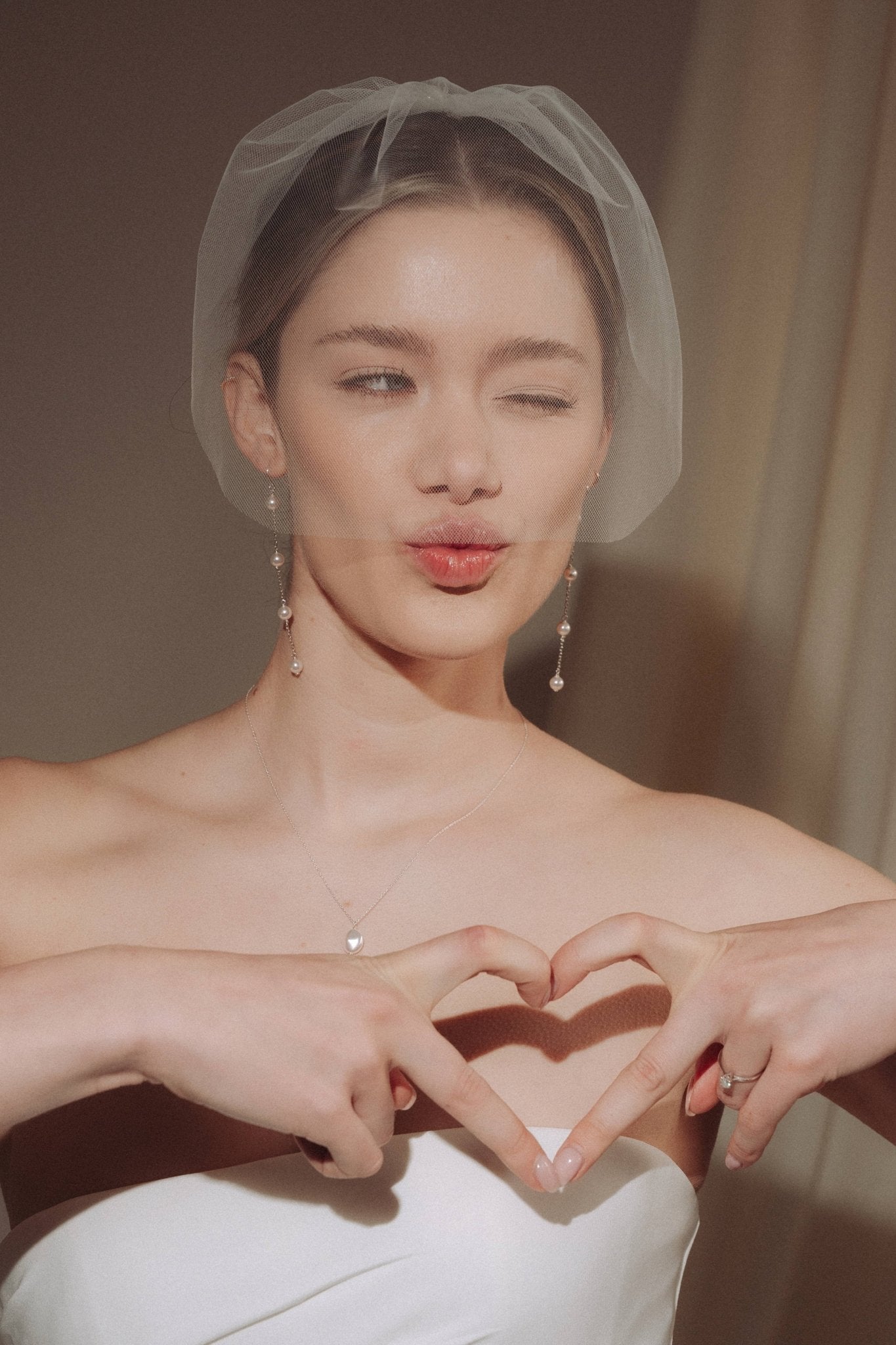 bride wears a sheer tulle birdcage style veil with long drop pearl earrings and a baroque coin pearl necklace
