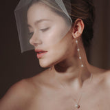 bride wears a sheer tulle birdcage style veil with long drop pearl earrings and a baroque coin pearl necklace