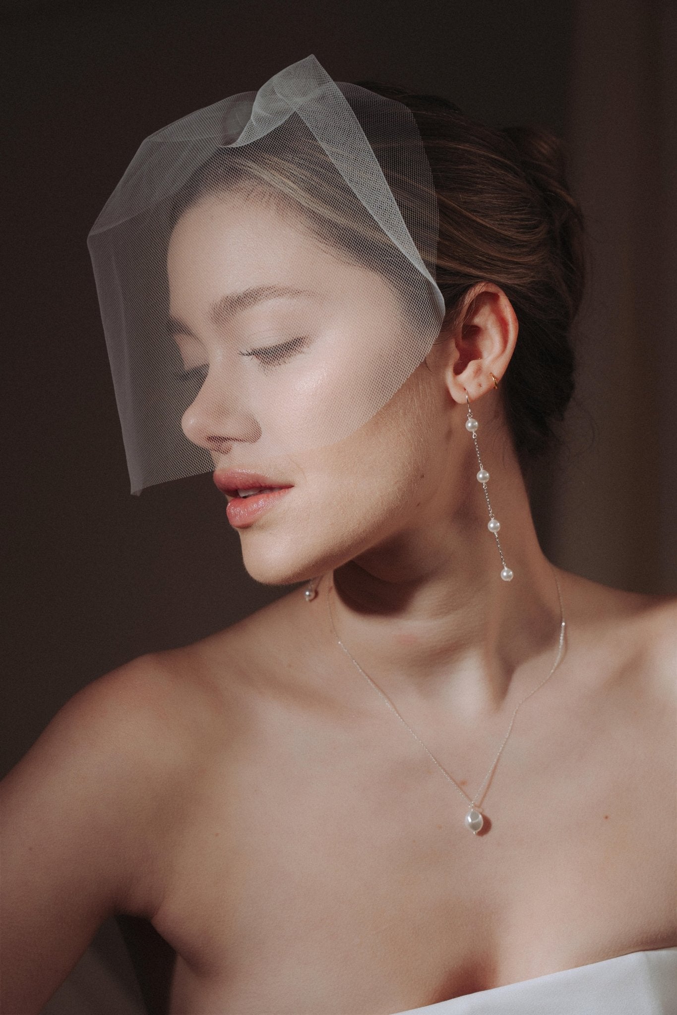 bride wears a sheer tulle birdcage style veil with long drop pearl earrings and a baroque coin pearl necklace