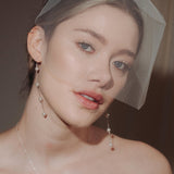 bride wears a sheer tulle birdcage style veil with long drop pearl earrings and a baroque coin pearl necklace