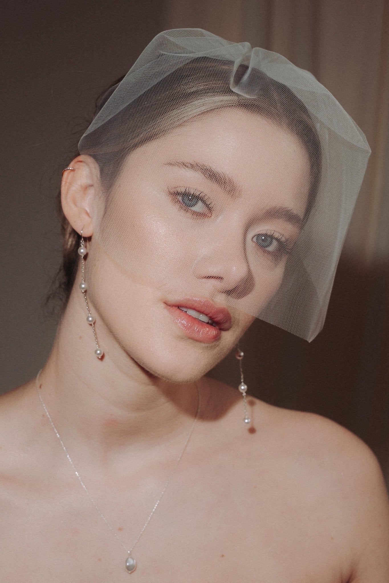 bride wears a sheer tulle birdcage style veil with long drop pearl earrings and a baroque coin pearl necklace