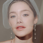 bride wears a sheer tulle birdcage style veil with long drop pearl earrings and a baroque coin pearl necklace
