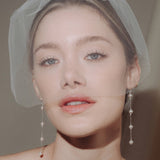 bride wears a sheer tulle birdcage style veil with long drop pearl earrings and a baroque coin pearl necklace