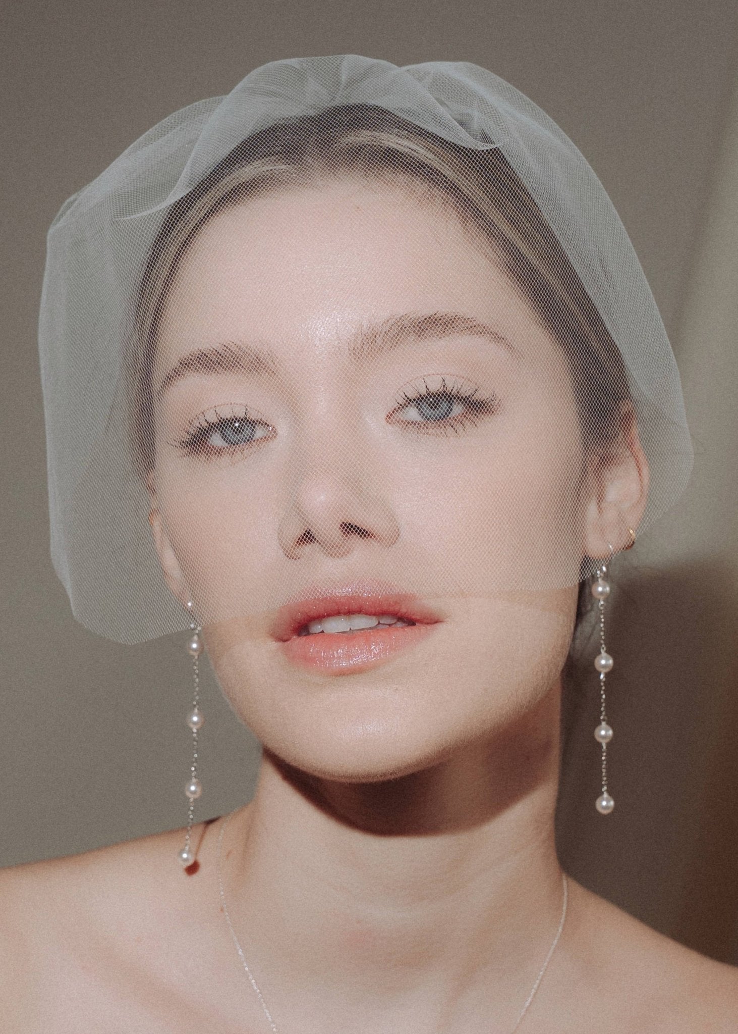 bride wears a sheer tulle birdcage style veil with long drop pearl earrings and a baroque coin pearl necklace