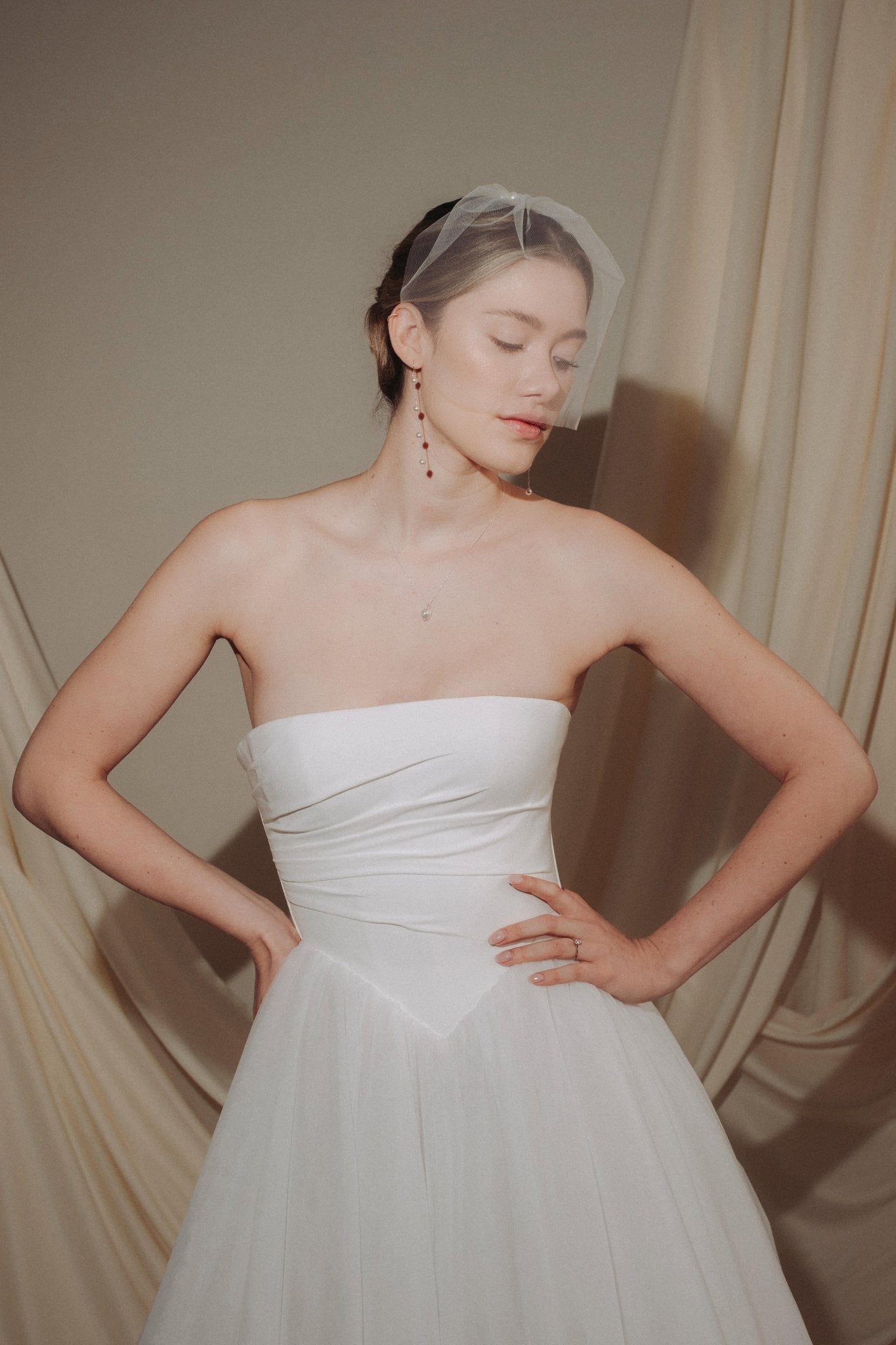 bride wears a sheer tulle birdcage style veil with long drop pearl earrings and a baroque coin pearl necklace