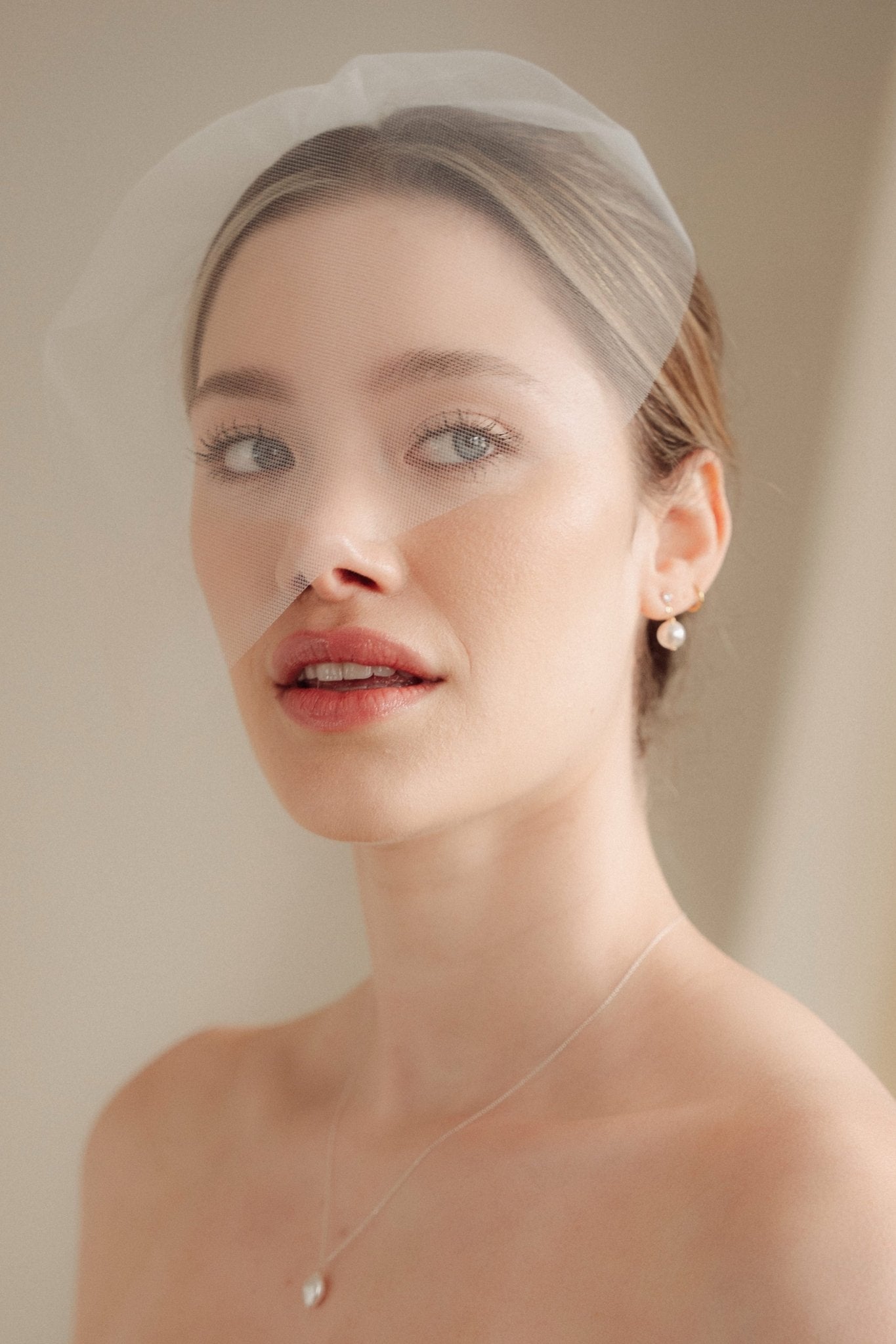 bride wears a sheer tulle birdcage style veil with small crystal and pearl stud drop earrings and a baroque coin pearl necklace