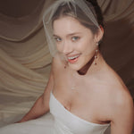 bride wears a sheer tulle birdcage style veil with long drop pearl earrings and a baroque coin pearl necklace