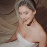bride wears a sheer tulle birdcage style veil with long drop pearl earrings and a baroque coin pearl necklace