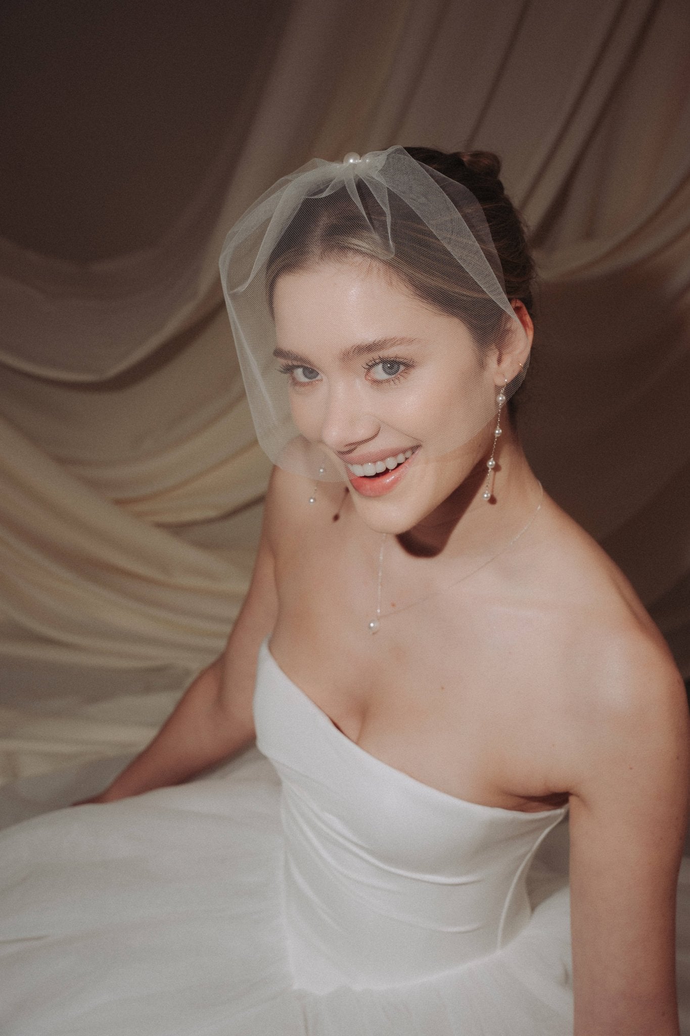 bride wears a sheer tulle birdcage style veil with long drop pearl earrings and a baroque coin pearl necklace
