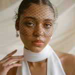 Black bride wears a black mask style Birdcage Veil with statement pearl earrings and a halterneck wedding dress.