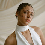 a bride wears a black mask style Birdcage Veil with statement pearl earrings and a halterneck wedding dress.