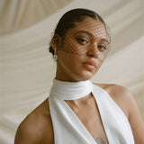 a bride wears a black mask style Birdcage Veil with statement pearl earrings and a halterneck wedding dress.