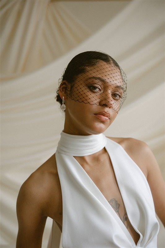 a bride wears a black mask style Birdcage Veil with statement pearl earrings and a halterneck wedding dress.