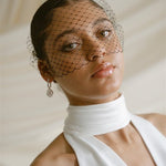 Black bride wears a black Birdcage Veil with statement pearl earrings and a halterneck wedding dress.