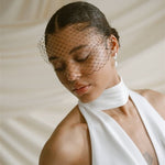 Black bride wears a black mask style Birdcage Veil with statement pearl earrings and a halterneck wedding dress.