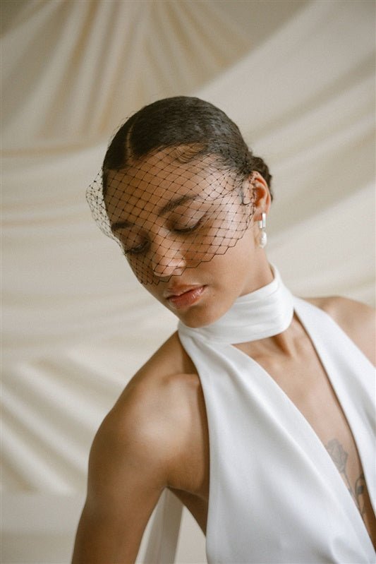 Black bride wears a black mask style Birdcage Veil with statement pearl earrings and a halterneck wedding dress.