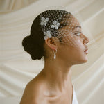 A black bride wears a full gathered birdcage veil with three ivory silk flower hair pins at each side above the ear.
