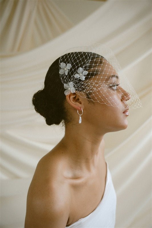 A black bride wears a full gathered birdcage veil with three ivory silk flower hair pins at each side above the ear.
