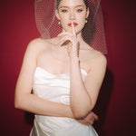 Bride wearing a white dress and long blusher length birdcage veil against a red background
