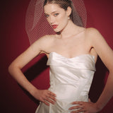 Bride wearing a white dress and long blusher length birdcage veil against a red background