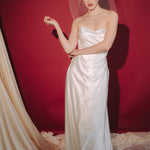 Bride wearing a white dress and long blusher length birdcage veil against a red background