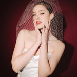 Bride wearing a white dress and long blusher length birdcage veil against a red background