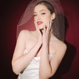 Bride wearing a white dress and long blusher length birdcage veil against a red background