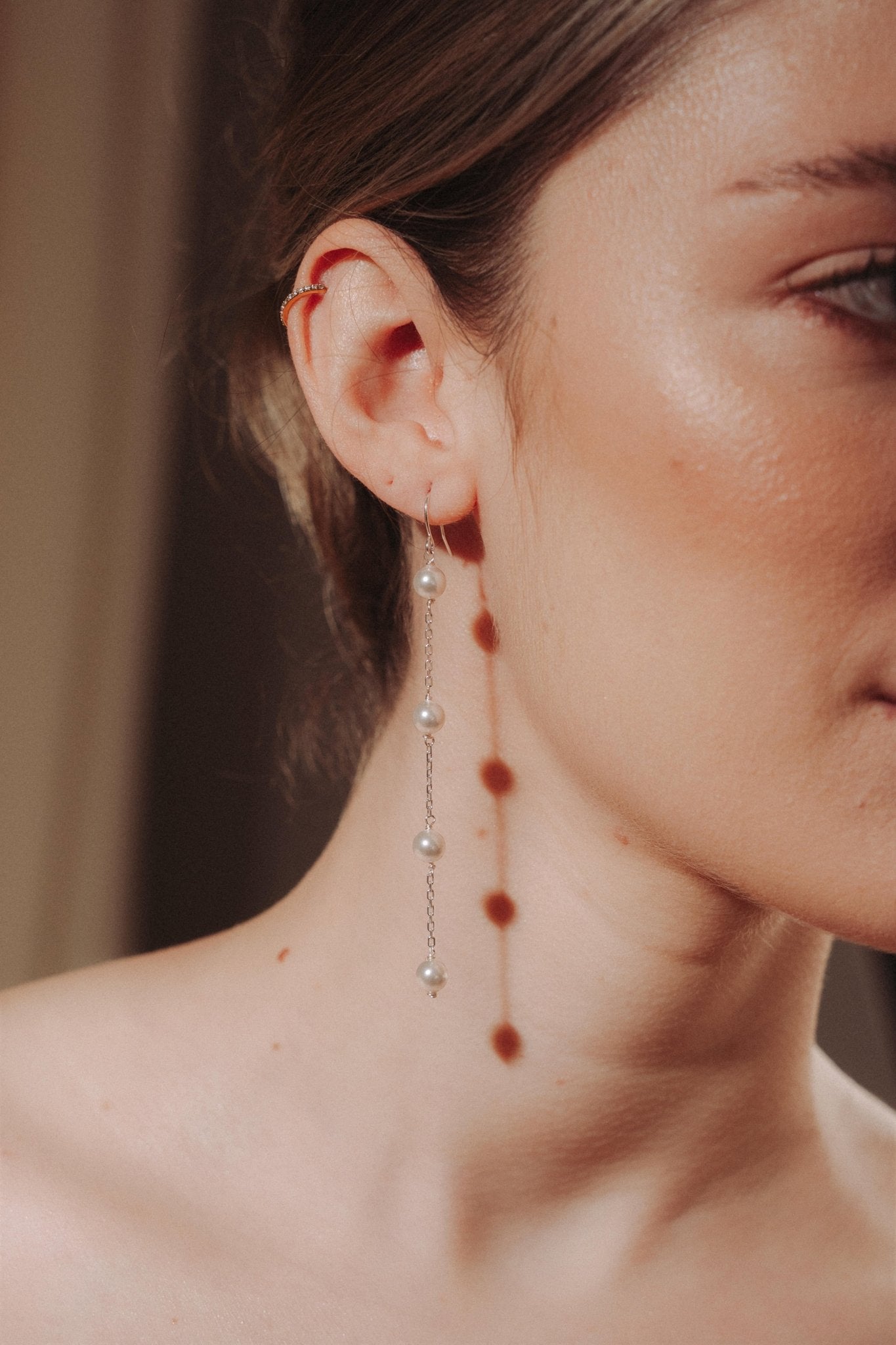 Close-up of a woman wearing a long delicate earring with four dangling pearl.