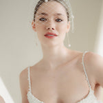 A bride wears a merry widow birdcage veil with vintage style chenille dots gold long crystal & baroque pearl drop earrings with a birdcage veil