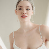 A bride wears a merry widow birdcage veil with vintage style chenille dots gold long crystal & baroque pearl drop earrings with a birdcage veil
