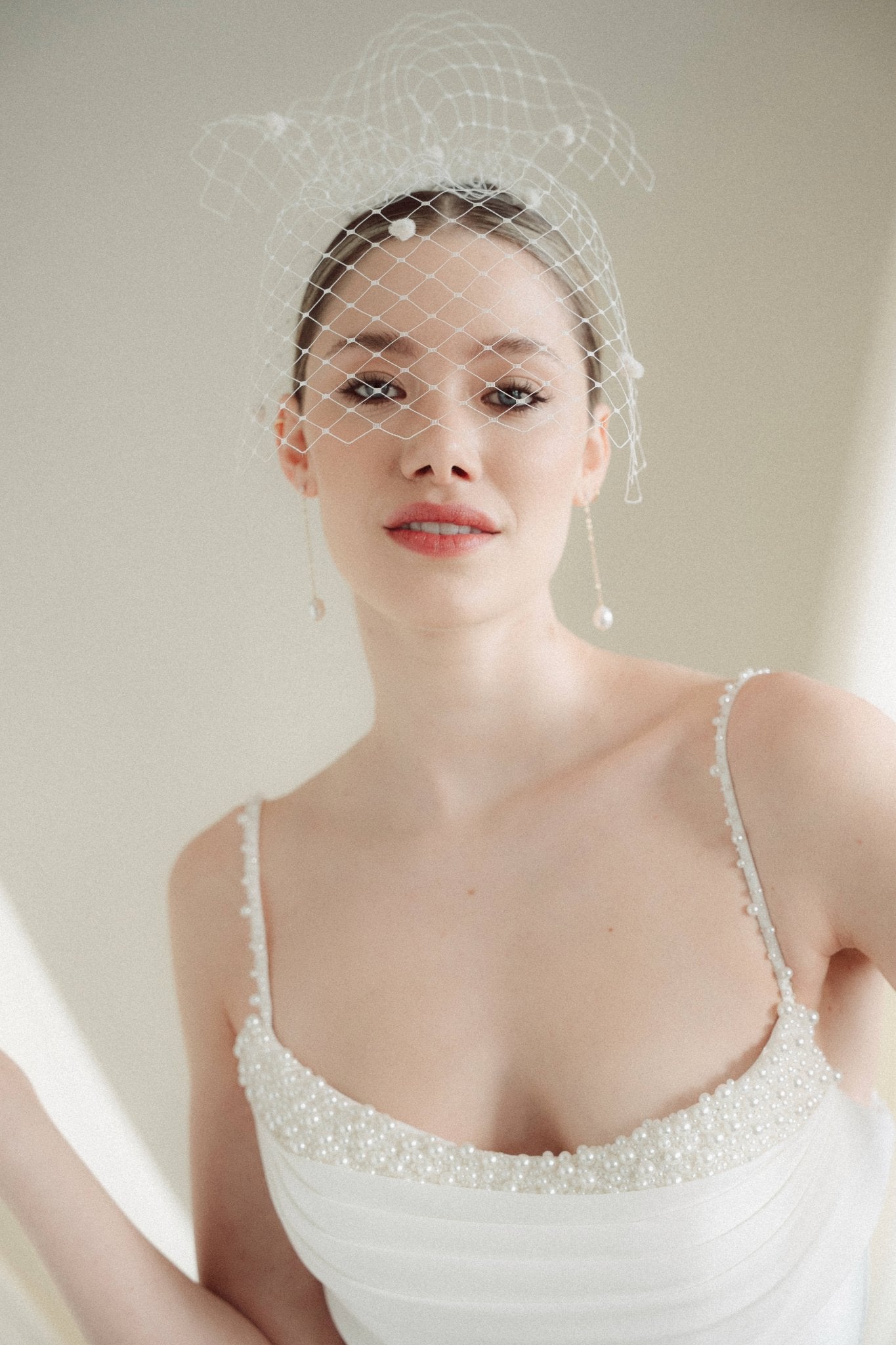 A bride wears a merry widow birdcage veil with vintage style chenille dots gold long crystal & baroque pearl drop earrings with a birdcage veil