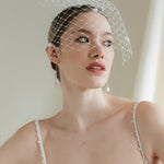 A bride wears a merry widow birdcage veil with vintage style chenille dots gold long crystal & baroque pearl drop earrings with a birdcage veil