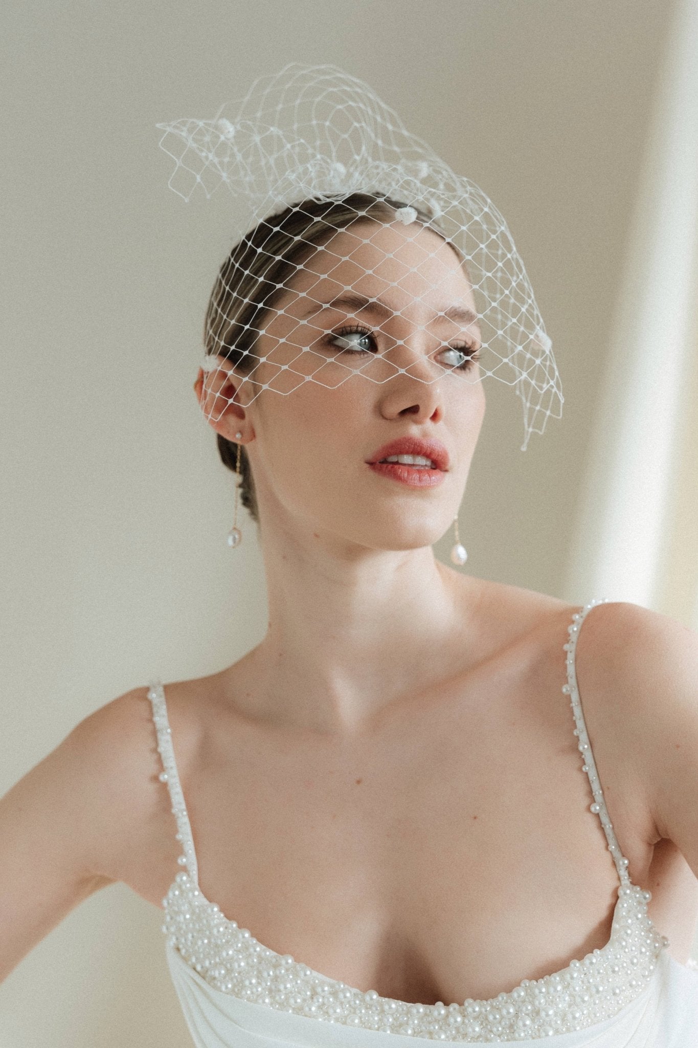 A bride wears a merry widow birdcage veil with vintage style chenille dots gold long crystal & baroque pearl drop earrings with a birdcage veil