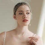 A bride wears a merry widow birdcage veil with vintage style chenille dots gold long crystal & baroque pearl drop earrings with a birdcage veil