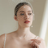 A bride wears a merry widow birdcage veil with vintage style chenille dots gold long crystal & baroque pearl drop earrings with a birdcage veil