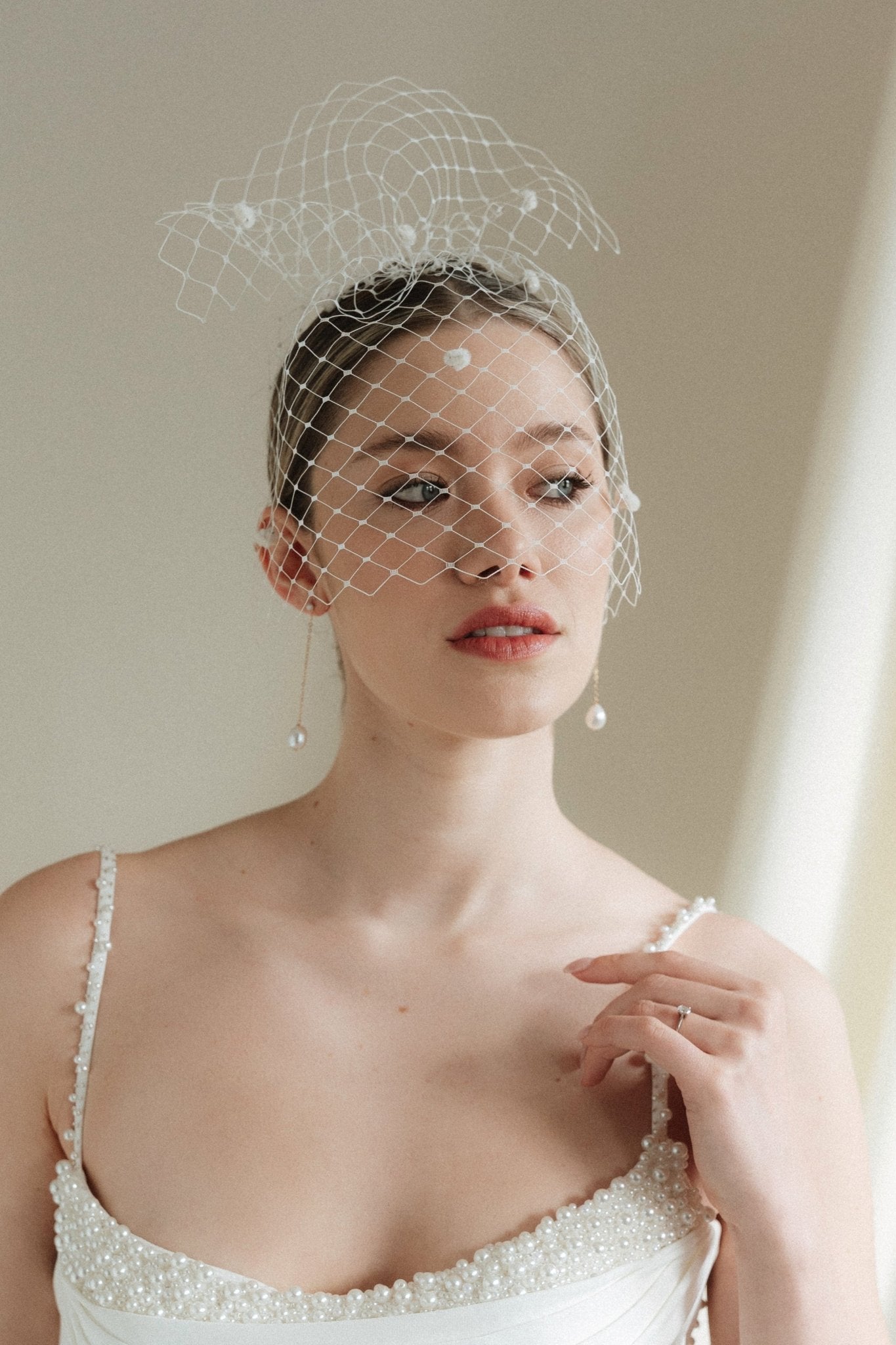 A bride wears a merry widow birdcage veil with vintage style chenille dots gold long crystal & baroque pearl drop earrings with a birdcage veil