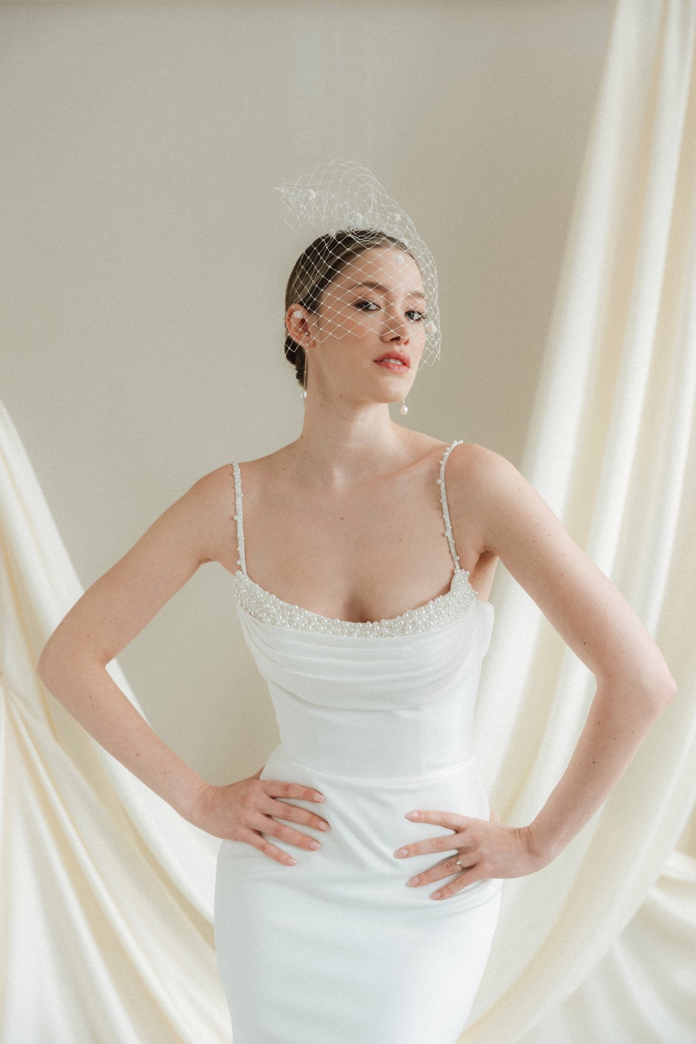 Bride wearing a white wedding dress with a chenille dot Merry Widow wedding veil against an ivory draped background