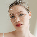 A bride wears a merry widow birdcage veil with vintage style chenille dots gold long crystal & baroque pearl drop earrings with a birdcage veil