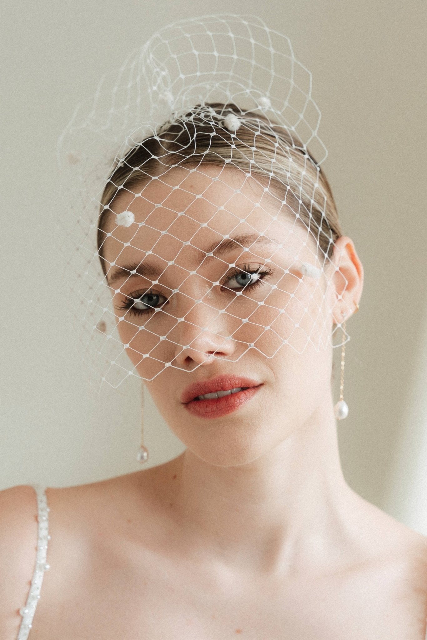 A bride wears a merry widow birdcage veil with vintage style chenille dots gold long crystal & baroque pearl drop earrings with a birdcage veil