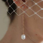 A bride wears gold long crystal & baroque pearl drop earrings